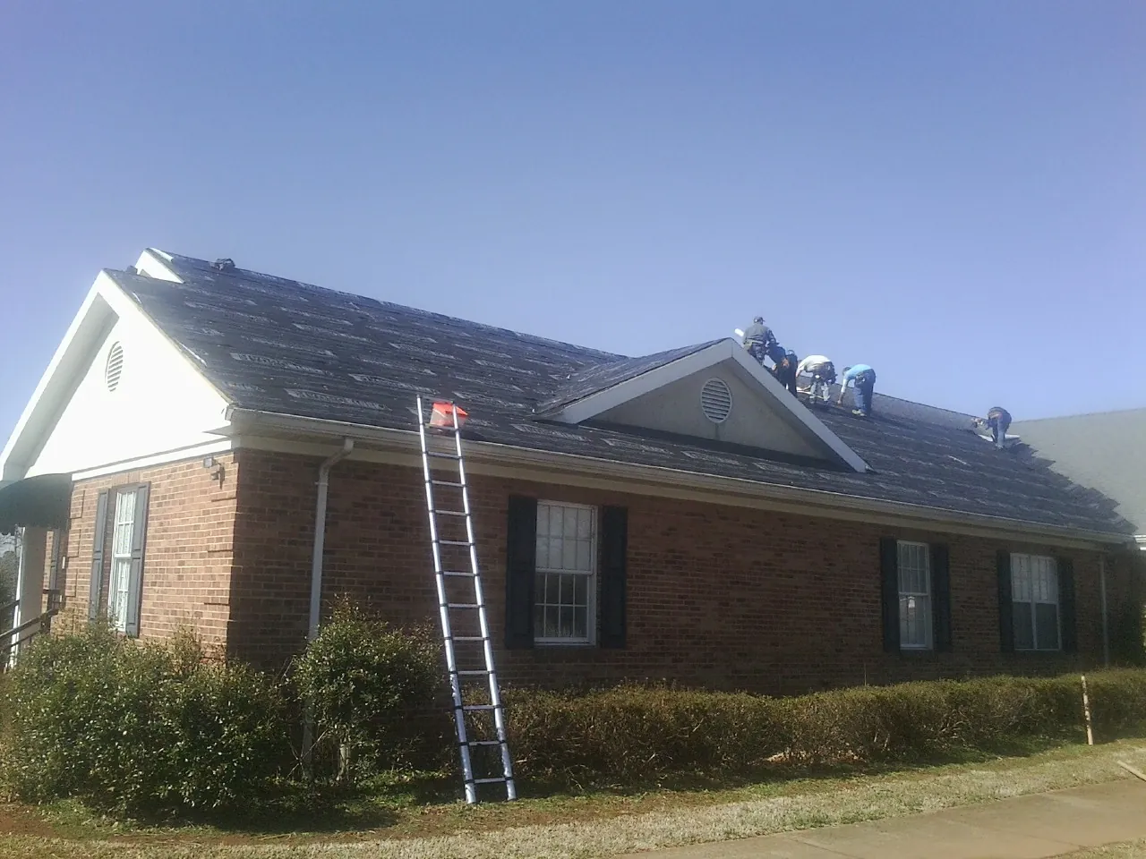 Crew tearing shingles off a brick ranch roof with a ladder set — Metal Roof Repair work by our crew in Howard Beach
