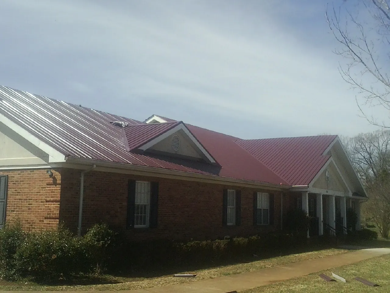 Red metal roof with gabled entries on a long brick building, from a Hail Damage Roof Repair job in Howard Beach