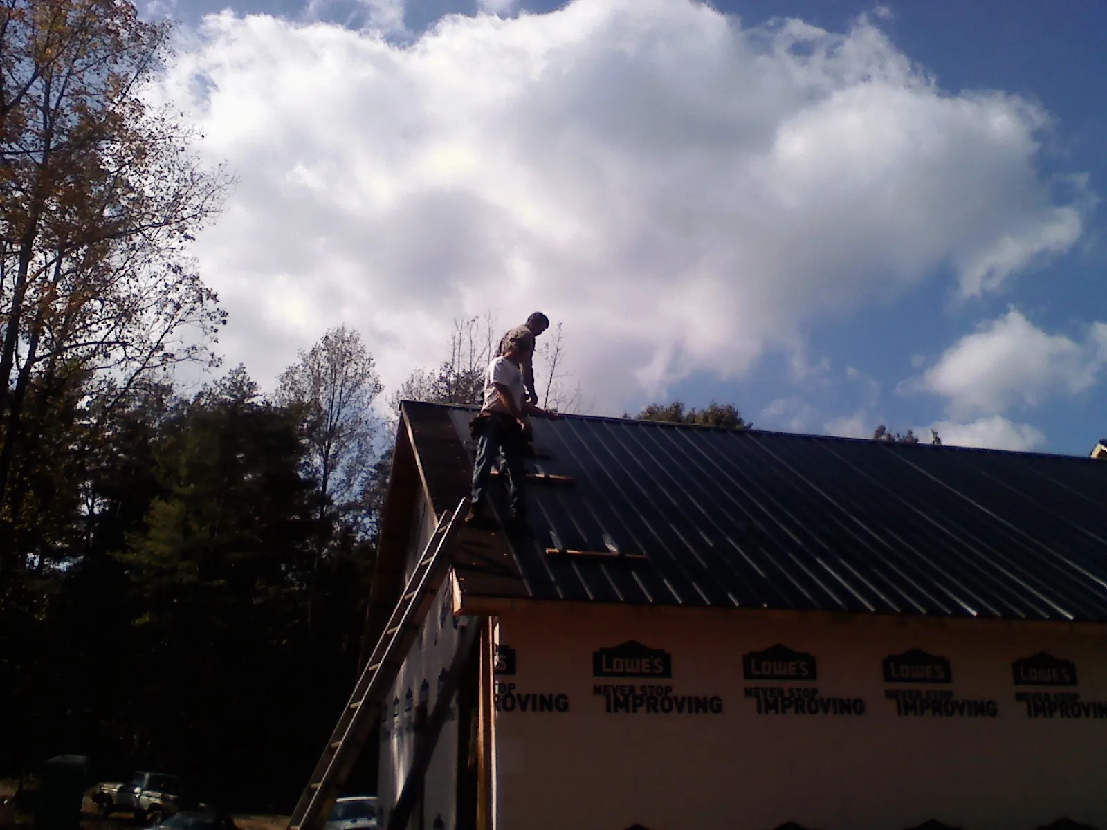Roofer fastening dark metal panels high against a cloudy sky, from a Roof Inspection job in Howard Beach