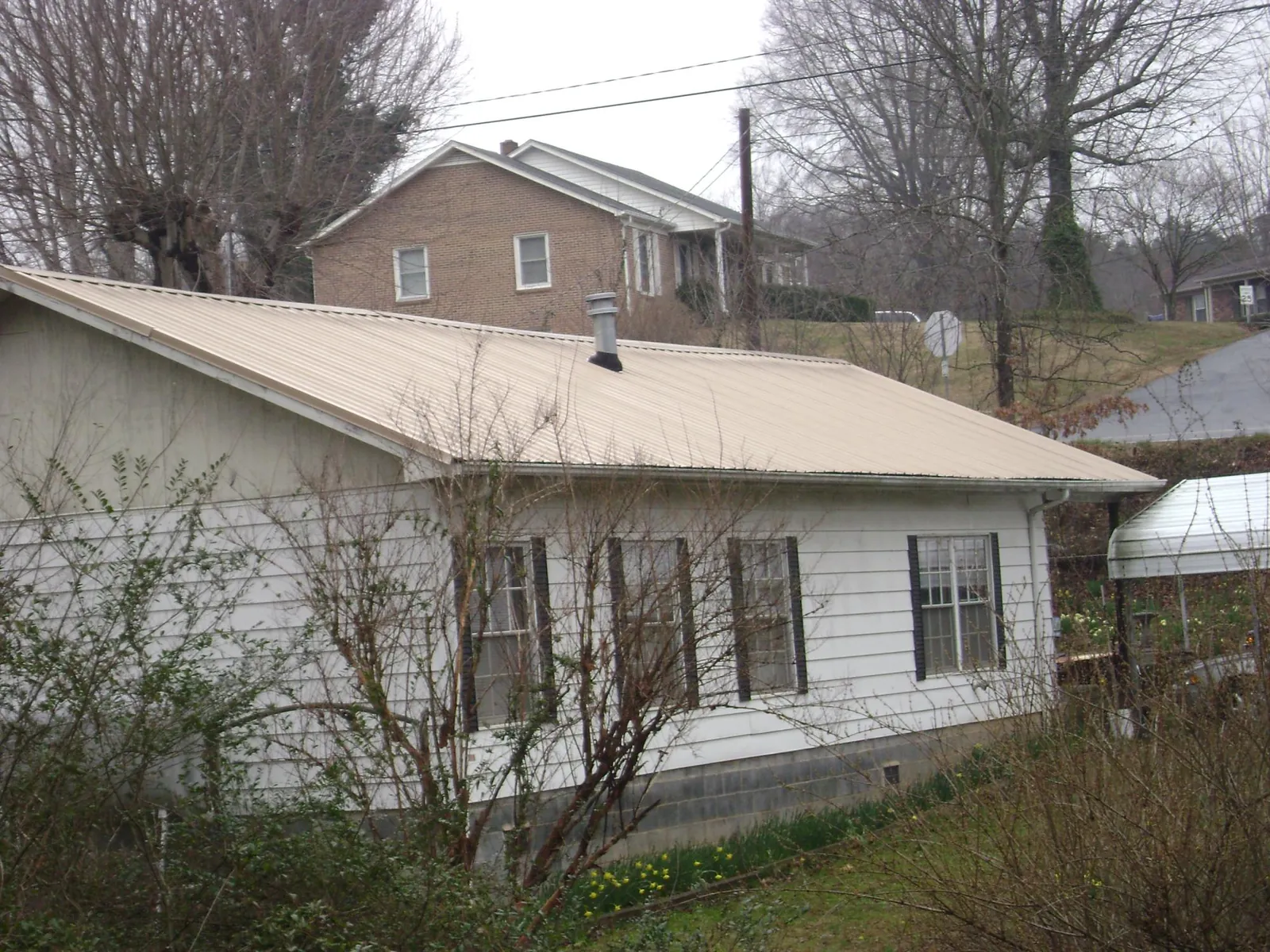 Tan metal roof on a white sided house set into a hillside — Commercial Roofing by Roofing Brothers in Howard Beach